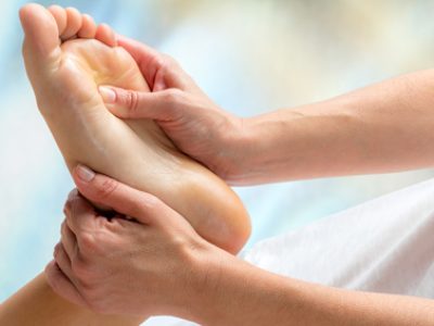 Reflexologist doing treatment on foot. Macro close up of hands applying pressure on foot against colorful background.
